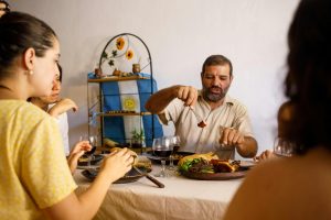 A family gathered around a table enjoying a traditional Argentine asado meal, with a man serving meat while others engage in conversation. In the background, an Argentine flag and rustic decor add cultural ambiance to the scene.