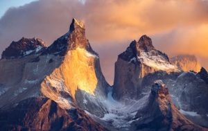 The iconic peaks of Cuernos del Paine in Torres del Paine National Park, Chile, illuminated by golden light at sunrise with dramatic clouds in the sky.