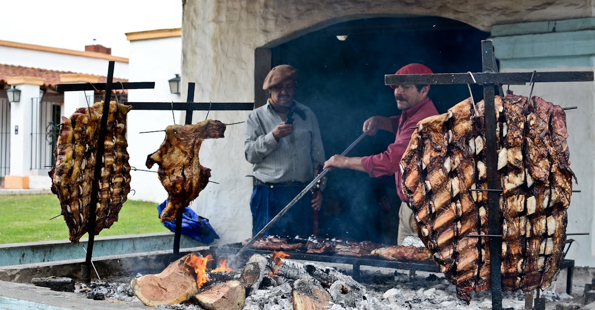 Argentine men preparing traditional asado with meats grilling over open flame outdoors.