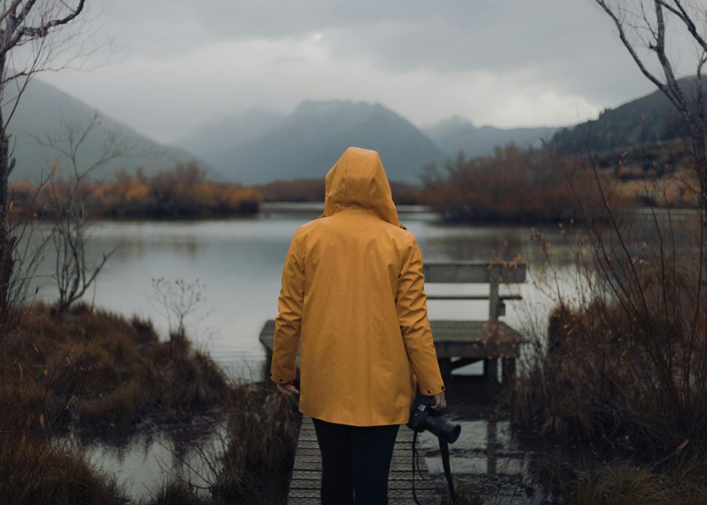 A person in a yellow raincoat walks by Lake Wakatipu in Glenorchy, New Zealand, on a drizzly autumn day.