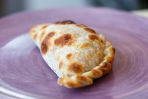 Close-up of a freshly baked Argentine empanada on a purple plate, showcasing authentic texture.