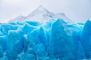 A stunning view of a vibrant blue glacier set against snow-capped mountains, showcasing winter's beauty.